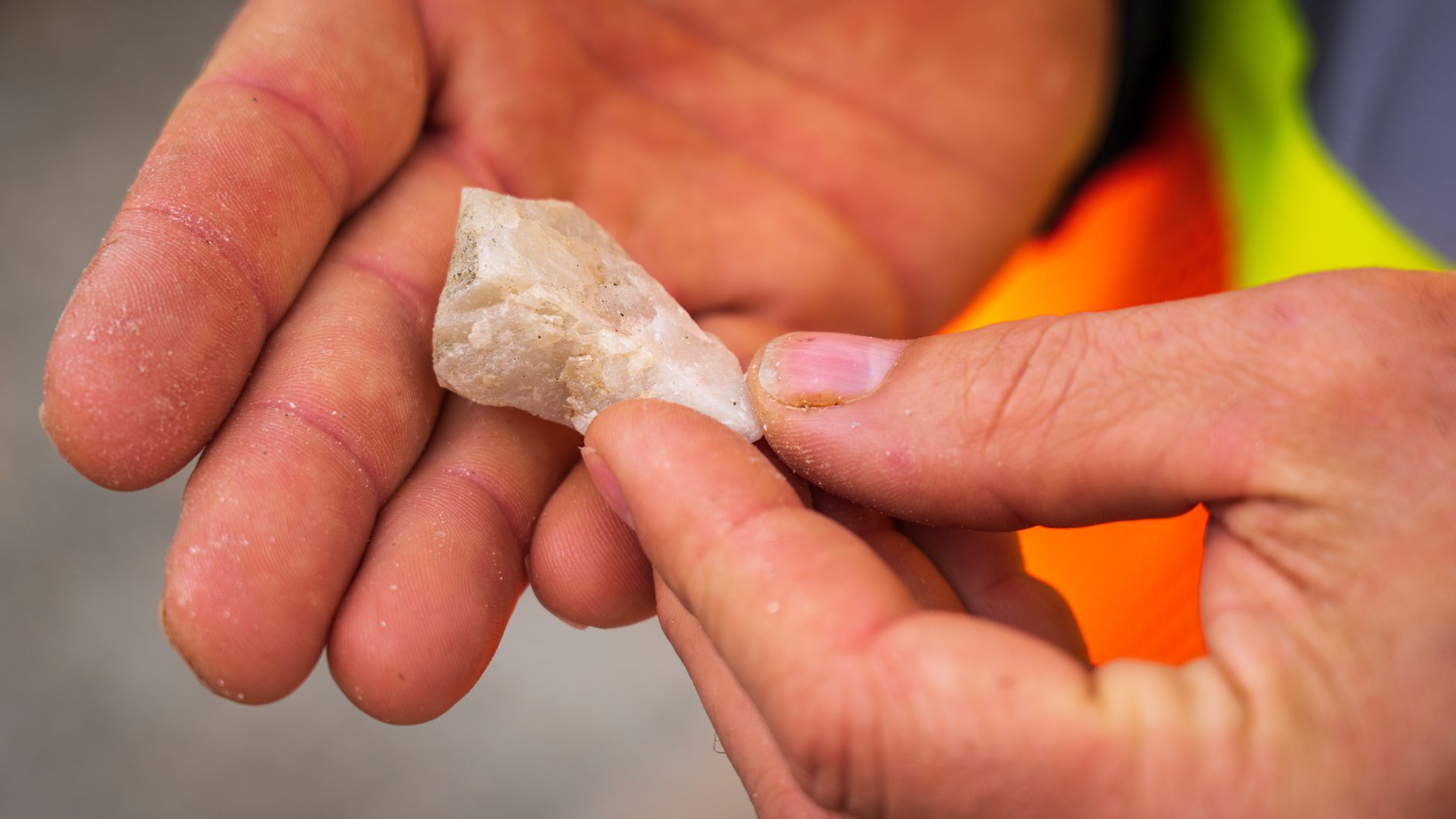 a person using a 10x loupe to inspect a rough mineral in the field